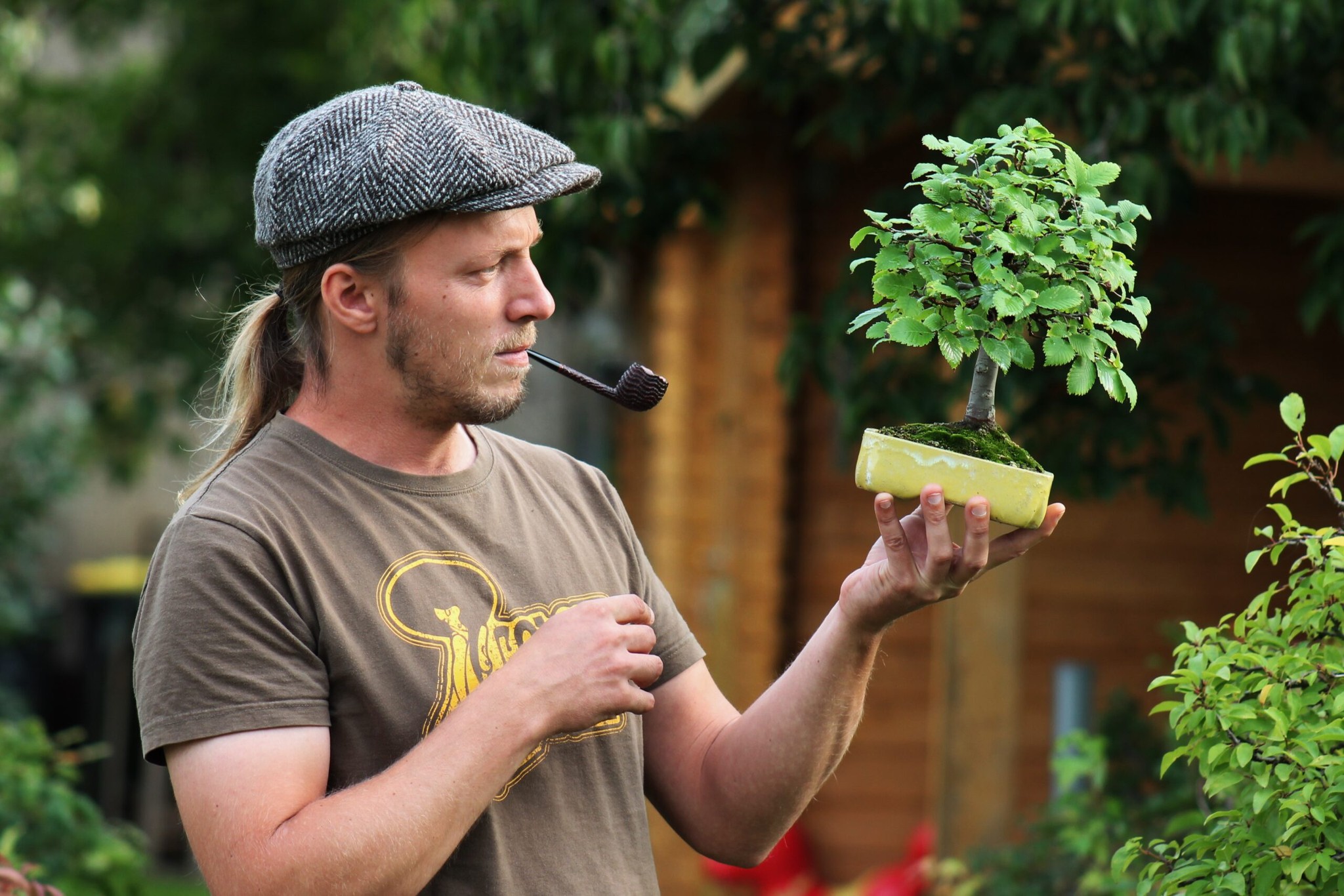 Tobias Höse im Profil mit Pfeife, einen kleinen Bonsai-Baum haltend